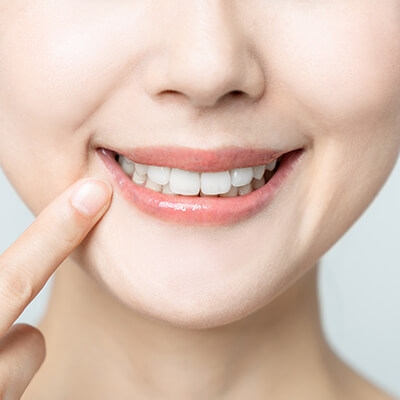 A woman pointing at her teeth while smiling after her restorative dentistry procedure