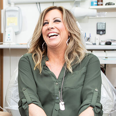 A female patient laughing while waiting to receive restorative dentistry and sitting in the dentist chair